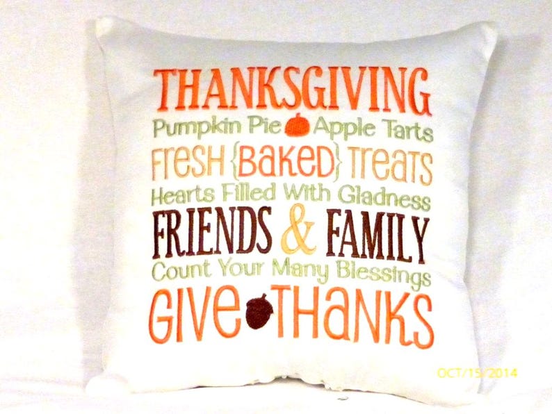 Fall pillow has a white background and subway tile style embroidered words.   The 1st line is, THANKSGIVING, in orange, 2nd line in small green embroidery is, Pumpkin Pie a orange pumpkin and apple tarts, 3rd line Fresh Baked Treats in gold, 4th line Hearts filled with gladness in green, 5th in a large font and brown thread is Friends &  Family, 6 in small green letter is Count your many blessings, 7 in large orange is Give Thanks with a  brown acorn between the words.