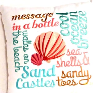 A 12x12 white embroidered pillow with coral shells in the center and with beach sayings embroidered on the front in Coral, sandy brown, and Aqua.  Sayings include, message in a bottle, Sand Castles, sandy toes, cool ocean breeze, walks on the beach, and sea shells.