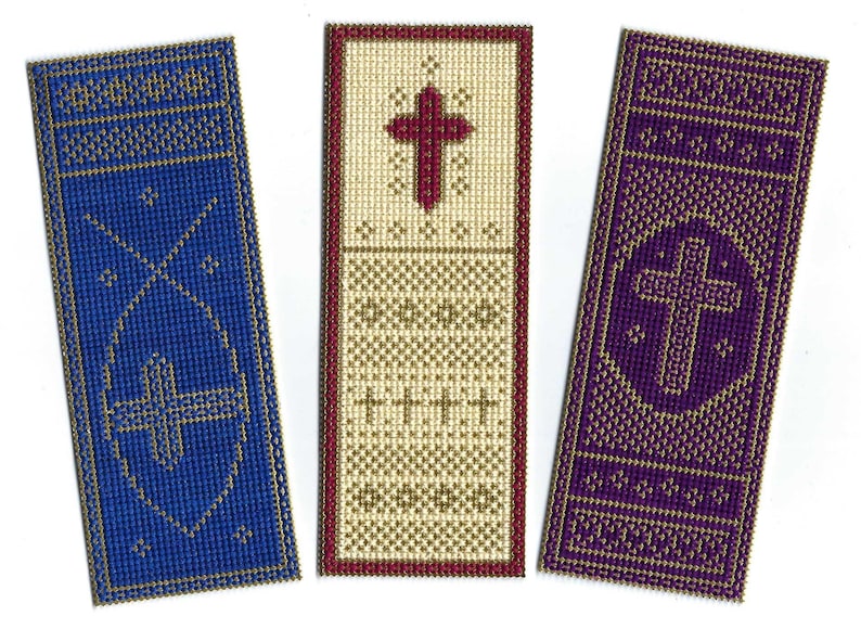 May include: Three embroidered bookmarks with gold trim. The bookmark on the left is blue with a gold cross. The middle bookmark is cream with a red cross and gold trim. The bookmark on the right is purple with a gold cross in a circle.