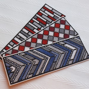 Op de afbeelding: Drie handgemaakte bladwijzers met verschillende geometrische patronen. De bovenste bladwijzer heeft een rood en grijs baksteenpatroon, de middelste bladwijzer heeft een rood en grijs geruit patroon en de onderste bladwijzer heeft een blauw, grijs en wit chevronpatroon.