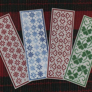 Puede incluir: Cuatro marcapáginas hechos a mano con punto de cruz con diferentes diseños. Los marcapáginas son blancos con bordados rojos, azules y verdes. Los diseños incluyen copos de nieve, corazones y hojas.