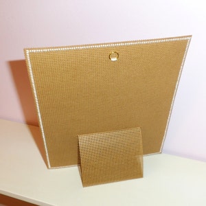 以下が含まれることがあります： 背面に白い縁取りと金色のリングが付いた茶色のキャンバス。キャンバスは同じ素材のスタンドの上に置かれています。