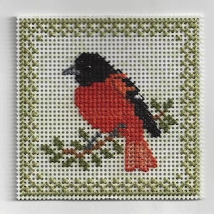 May include: A cross-stitch design of a red and black bird perched on a green branch. The bird is surrounded by a green border.
