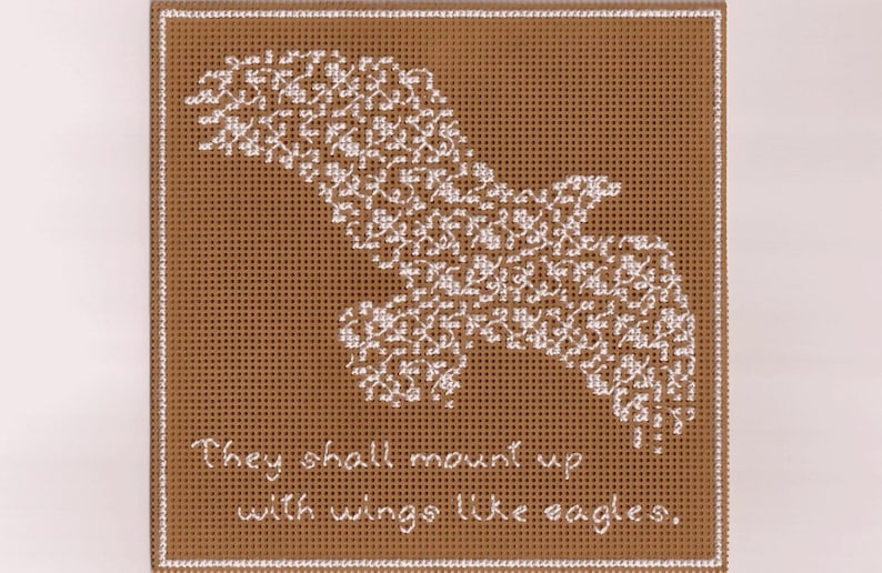 以下が含まれることがあります： 茶色のキャンバスに、白い刺繍の鷲と「They shall mount up with wings like eagles.」というテキストが書かれています