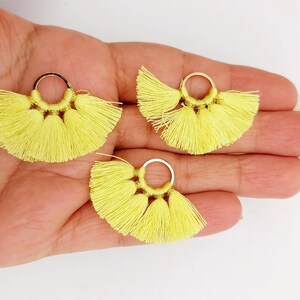 Può includere: Tre orecchini con nappe gialle e anelli dorati. Le nappe sono fatte di sottili fili di filo e sono disposte a forma di ventaglio.