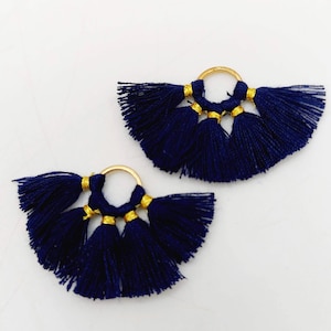 Può includere: Un paio di orecchini a nappa blu con cerchi dorati. Ogni orecchino ha tre nappe con dettagli dorati.