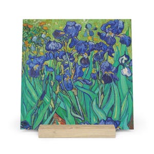 May include: A square print of Vincent van Gogh's "Irises" painting, featuring vibrant blue irises with green leaves against a green and yellow background. The artwork is displayed on a wooden stand, showcasing the floral subject matter.