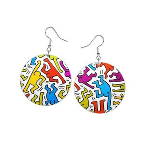 May include: A pair of round earrings featuring a colorful design of stylized human figures in yellow, red, blue, green, and purple on a white background. The earrings have silver-colored hooks.