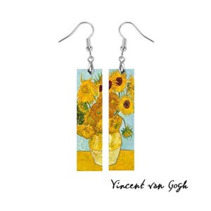 May include: A pair of dangle earrings featuring a print of Van Gogh's "Sunflowers" painting. The earrings have a light blue background with yellow sunflowers in a yellow vase. The text "Vincent van Gogh" is below the earrings.