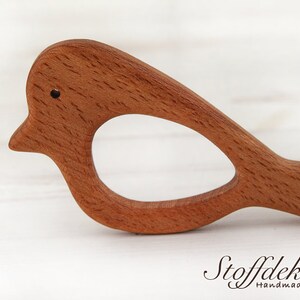 May include: A wooden bird-shaped teether for babies. The teether is made of beech wood and is finished with natural bio-linseed oil. It is certified as safe for babies and is made with sustainable materials.