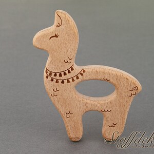 May include: A wooden llama teether with a brown and white design. The teether is made of beech wood and is safe for babies. The teether is shaped like a llama with a long neck and a small head. The teether has a small hole in the middle for a baby to hold onto.
