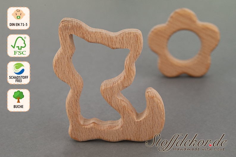 May include: Two wooden teethers for babies. One is shaped like a flower with a hole in the center. The other is shaped like a squiggly line with a hole in the center. Both are made of natural wood.