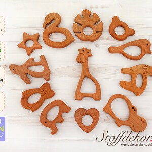 May include: A set of 12 wooden teethers shaped like animals, including a giraffe, a bird, a hippopotamus, a turtle, an elephant, a star, a leaf, and a heart. The teethers are made of natural wood and are safe for babies to chew on. DIN EN 71-3, FSC, Schadstoff Frei, Buche, Bio Lein Ol.