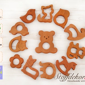 May include: A set of 12 wooden teethers in various animal shapes, including a bear, bird, cat, deer, and horse. The teethers are made of natural beech wood and are safe for babies. The teethers are handmade and come with the text "Stoffdekor.de Handmade with Love".