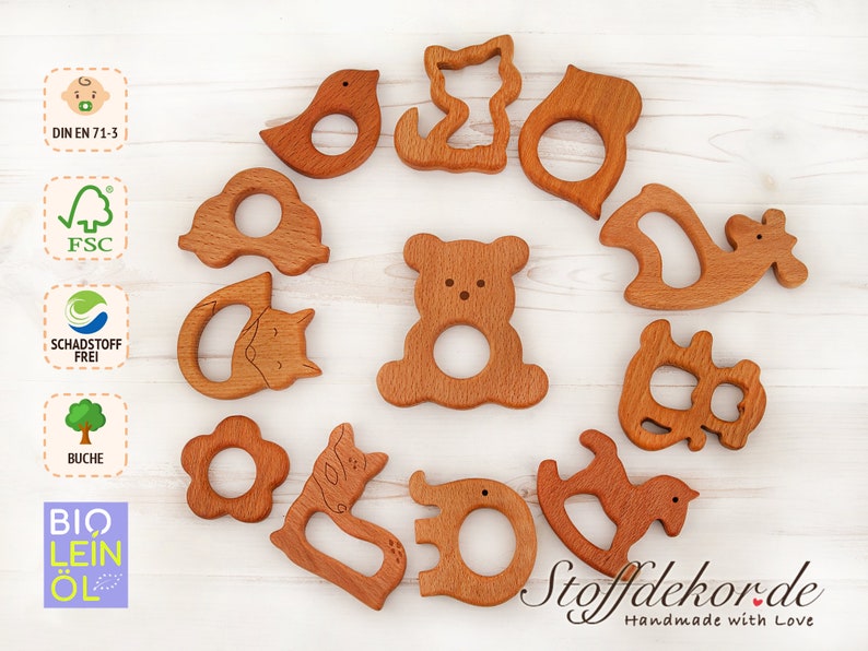May include: A set of 12 wooden teethers in various animal shapes, including a bear, bird, cat, deer, and horse. The teethers are made of natural beech wood and are safe for babies. The teethers are handmade and come with the text "Stoffdekor.de Handmade with Love".