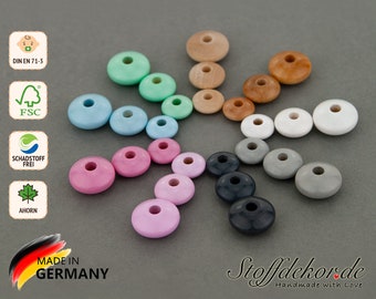 Könnte beinhalten: Sortiment aus Holzperlen in verschiedenen Farben, darunter rosa, blau, grün, grau und schwarz. Die Perlen sind in einem Kreis auf einem grauen Hintergrund angeordnet. Die Perlen sind alle rund und haben ein Loch in der Mitte. Der Text "Stoffdekor.de Handmade with Love" ist in der rechten unteren Ecke des Bildes sichtbar.