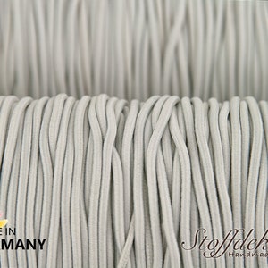 Pu&ograve; includere: Primo piano di un rotolo di cordoncino elastico grigio. Il cordoncino &egrave; prodotto in Germania ed &egrave; certificato secondo lo standard Oeko-Tex 100 e DIN EN 71-3.