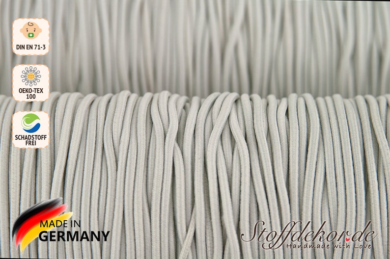 Pu&ograve; includere: Primo piano di un rotolo di cordoncino elastico grigio. Il cordoncino &egrave; prodotto in Germania ed &egrave; certificato secondo lo standard Oeko-Tex 100 e DIN EN 71-3.