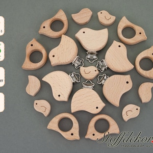 Könnte beinhalten: Ein Set mit 15 Holz-Beißringen in Vogelform mit einem Clip. Die Beißringe sind aus natürlichem Buchenholz gefertigt und für Babys sicher. Die Beißringe sind in verschiedenen Größen und Formen erhältlich, einige haben einen Ring für einen einfachen Griff. Die Beißringe sind eine großartige Möglichkeit, um das Zahnfleisch von Babys zu beruhigen und sensorische Stimulation zu bieten.