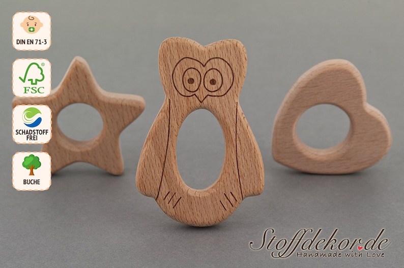 May include: Three wooden teethers in the shapes of a star, an owl, and a heart. The teethers are made of natural beech wood and are safe for babies to chew on. The teethers are labeled with the text "DIN EN 71-3", "FSC", "Schadstoff Frei", and "Buche".