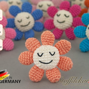 Könnte beinhalten: Eine Sammlung gehäkelter Blumenspielzeuge mit lächelnden Gesichtern. Die Blumen sind in verschiedenen Farben, darunter rosa, blau und orange. Die Blumen sind aus weichem Garn gefertigt und haben ein zartes, handgemachtes Aussehen.