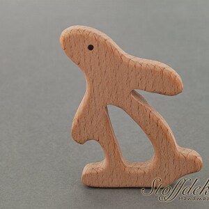 May include: A wooden bunny rabbit toy made from beech wood. The toy is unfinished and has a natural wood color. The toy is designed for babies and toddlers and is safe for chewing. The toy is made in Germany and is certified by the FSC and DIN EN 71-3.