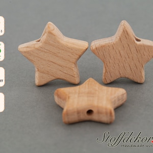 Puede incluir: Tres cuentas de madera en forma de estrella, cada una con un agujero en el centro. Las cuentas son de color marrón claro y tienen una veta de madera natural. Las cuentas están hechas de madera de haya y están certificadas por FSC y DIN EN 71-3.