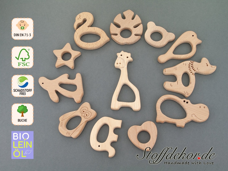 May include: A set of 12 wooden teethers shaped like animals, a star, a leaf, a heart, and a swan. The teethers are made of natural wood and are safe for babies. The teethers are labeled with the text "Stoffdekor.de Handmade with Love".