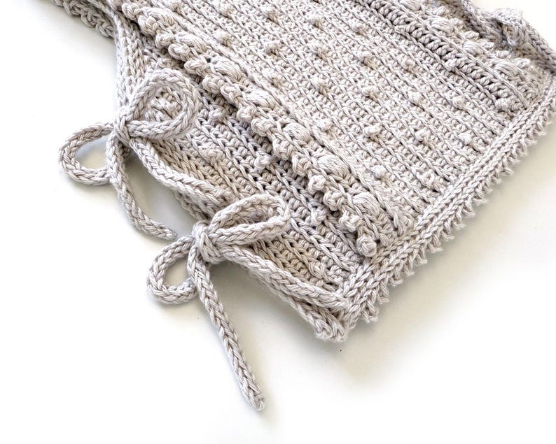 Peut inclure: Un article au crochet fait &agrave; la main, de couleur gris clair, avec un motif textur&eacute; et une bordure d&eacute;corative. L'article comporte deux ensembles de liens, chacun nou&eacute; en n&oelig;ud. Le crochet est d&eacute;taill&eacute; et semble doux et confortable.