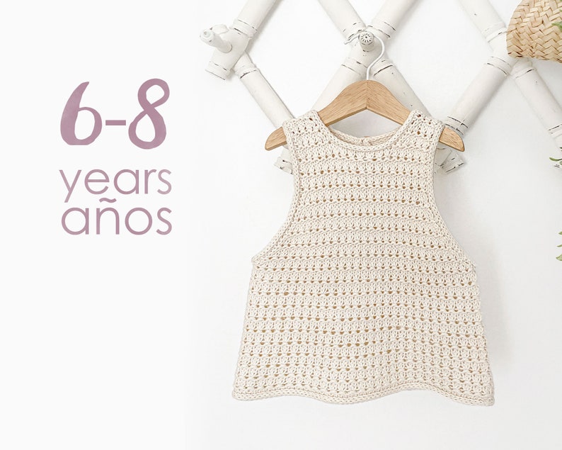 May include: A white crocheted sleeveless top for children, hanging on a wooden hanger. The top has a delicate openwork pattern. The text "6-8 years a&ntilde;os" is visible in the image.