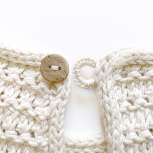 May include: Close-up of a white crocheted garment with a wooden button and a loop for fastening. The fabric is textured and has a woven appearance.