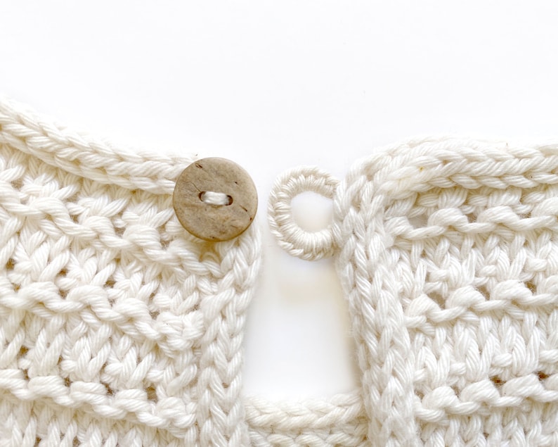 May include: Close-up of a white crocheted garment with a wooden button and a loop for fastening. The fabric is textured and has a woven appearance.