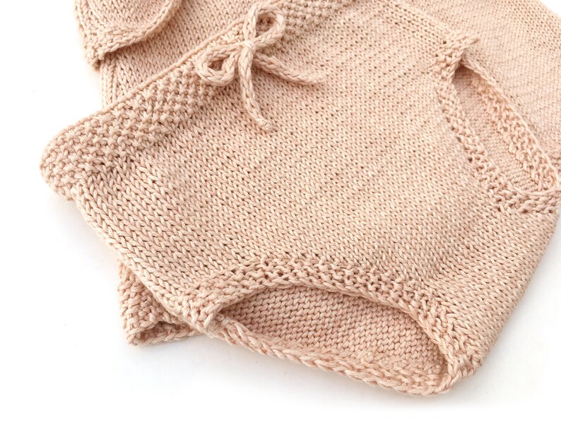 May include: A pair of knitted shorts in a light pink color. The shorts have a tie at the waist and are made of a soft, comfortable fabric.