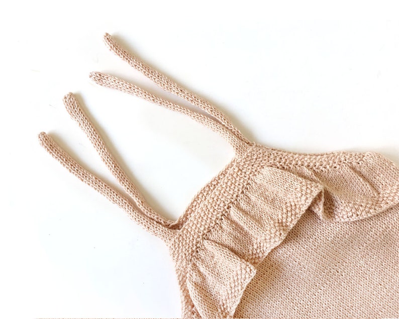 May include: A light pink knitted baby romper with ruffled straps. The romper is made of a soft, lightweight material and has a relaxed fit.