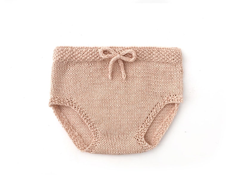 May include: A pair of knitted baby bloomers in a light pink color. The bloomers have a bow at the waist and a delicate lace trim.