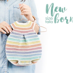 Pode incluir: Um macacão de crochê listrado em tons pastel, tamanho recém-nascido, preso em um cabide de cobre. O macacão apresenta decote redondo, design sem mangas e fechos de pressão. O texto na imagem diz "Newborn size talla".