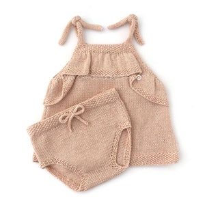May include: A knitted baby outfit in a light peach color. The outfit includes a sleeveless top with a ruffled neckline and matching shorts.