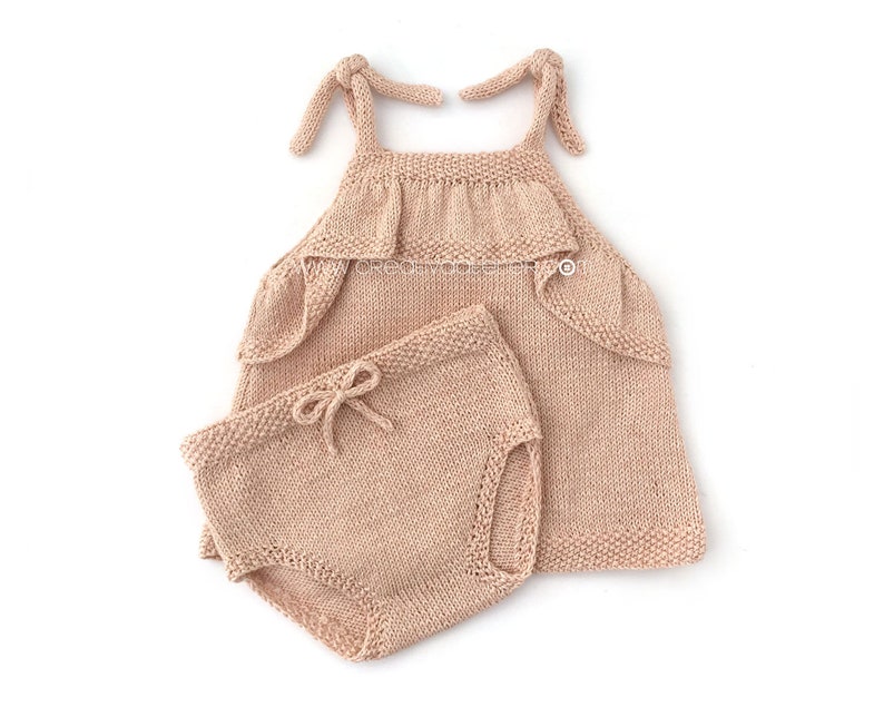 May include: A knitted baby outfit in a light peach color. The outfit includes a sleeveless top with a ruffled neckline and matching shorts.