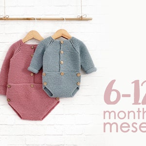 Könnte beinhalten: Zwei gestrickte Baby-Bodys, einer in Rosa und einer in Blau, hängen an einem Holz-Kleiderbügel. Die Bodys haben Knopfverschlüsse und sind mit "6-12 Monate meses" beschriftet.