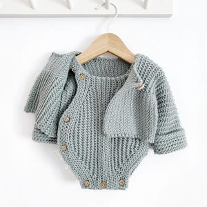 May include: A sage green knitted baby outfit with a matching hat and cardigan. The outfit features a button closure and is made of soft, comfortable material.