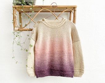 Könnte beinhalten: Ein cremefarbener Strickpullover mit einem Farbverlauf von Rosa zu Lila. Der Pullover hat einen runden Ausschnitt und lange Ärmel.