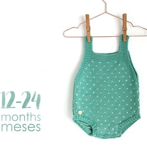 Puede incluir: Un body de bebé de punto color turquesa con lunares blancos, colgado de una percha de madera. El body está etiquetado con "12-24 meses meses".