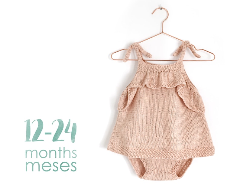 May include: A knitted baby romper with a ruffled neckline and straps. The romper is a light pink color and is hanging on a hanger. The text "12-24 months meses" is printed below the romper.
