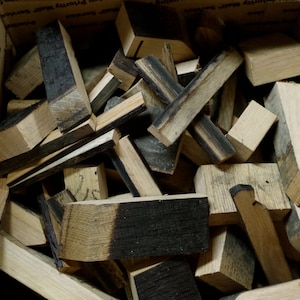 May include: A box filled with various sizes and shapes of wood pieces. The wood is a mix of light brown and dark brown, with some pieces having a charred black finish. The wood pieces appear to be from a barrel.