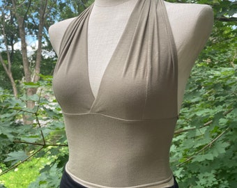 May include: A halter top in a light sage green color. The top is made of a soft, stretchy fabric and has a deep V-neckline. It is sleeveless and has a cropped length.