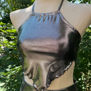 May include: A silver halter top with a ruffled hem. The top is made of a shiny, metallic fabric.