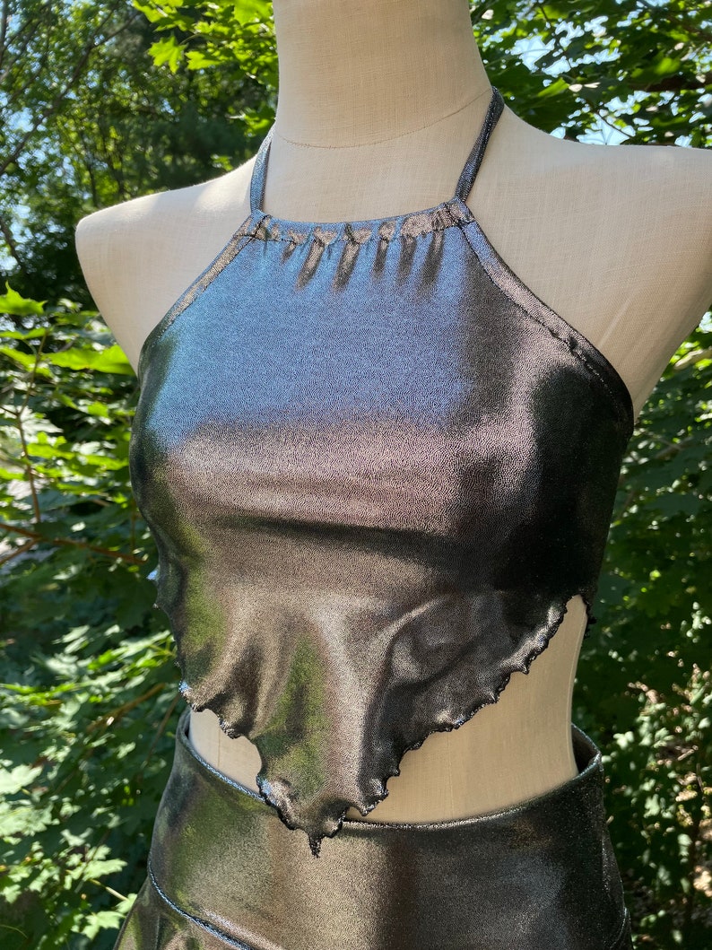 May include: A silver halter top with a ruffled hem. The top is made of a shiny, metallic fabric.