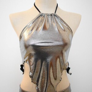 May include: A silver metallic halter top with a black adjustable strap. The top has a loose, flowing fit and a slightly asymmetrical hemline.