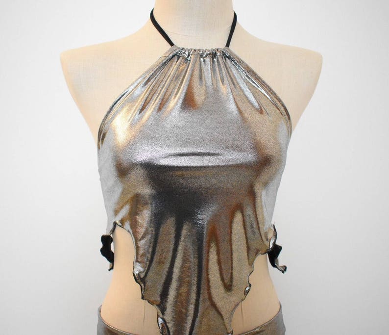 May include: A silver metallic halter top with a black adjustable strap. The top has a loose, flowing fit and a slightly asymmetrical hemline.
