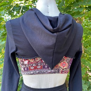 Peut inclure: Haut à capuche noir à manches longues avec un panneau de tissu à motifs coupé au dos. Le panneau de tissu présente un motif géométrique coloré.